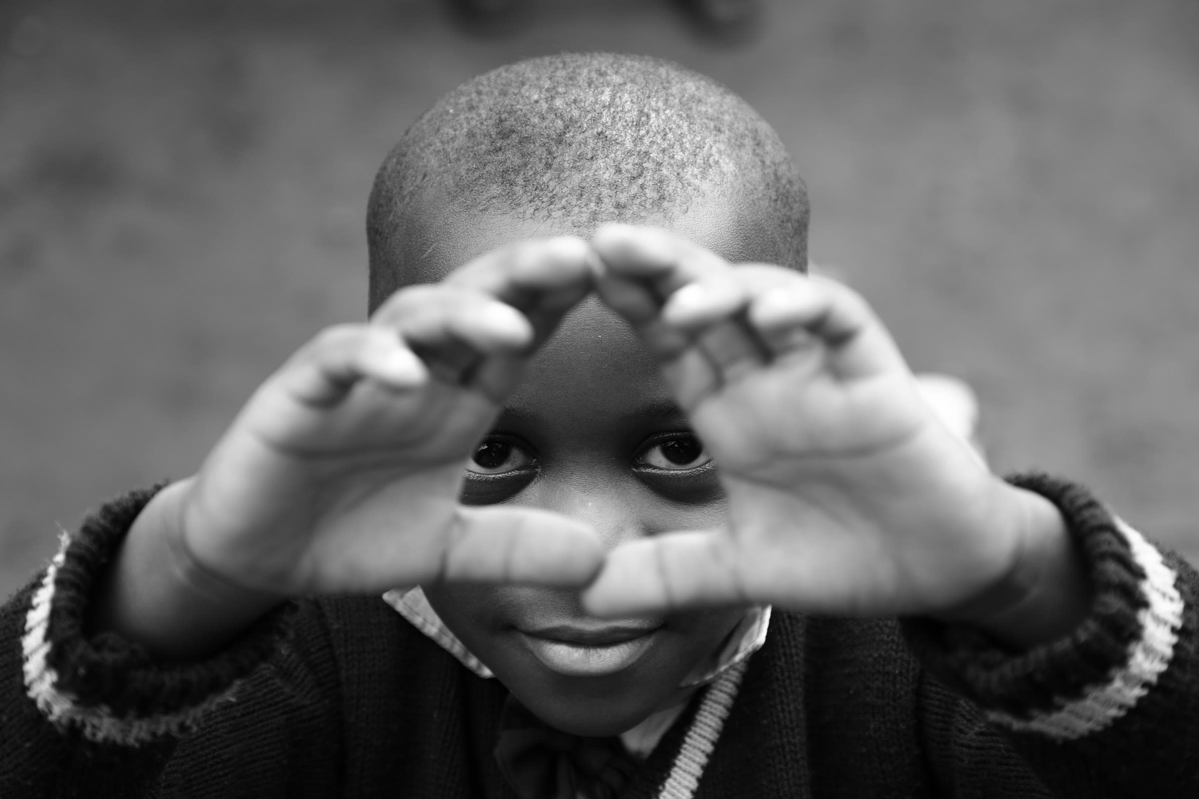 A child looking out through a triangle framed by their own hands, black and white