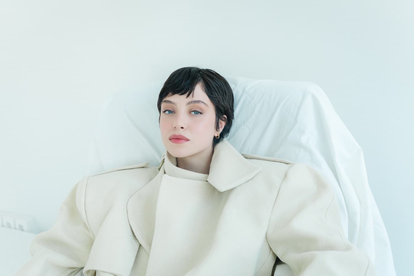 Beauty portrait in a cream wool coat, direct gaze against soft daylight