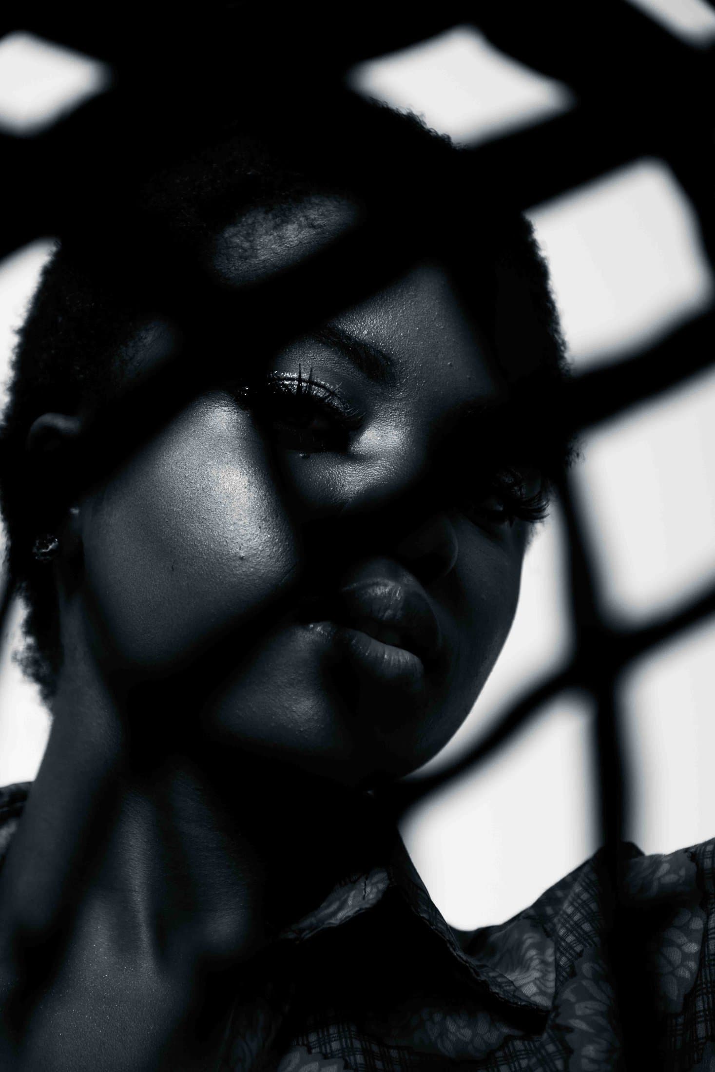 Window-lattice shadow grid across a dark-skinned face, one glint of light